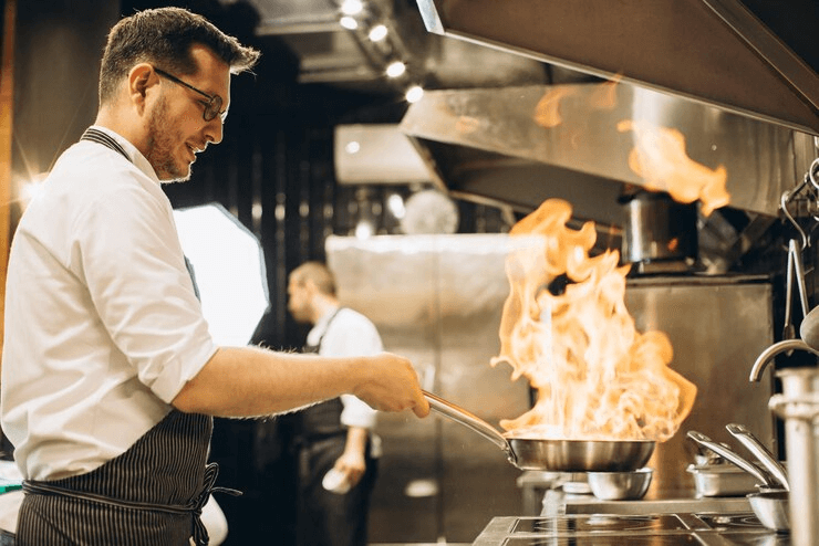 A chef handles a flaming pan over a commercial stove