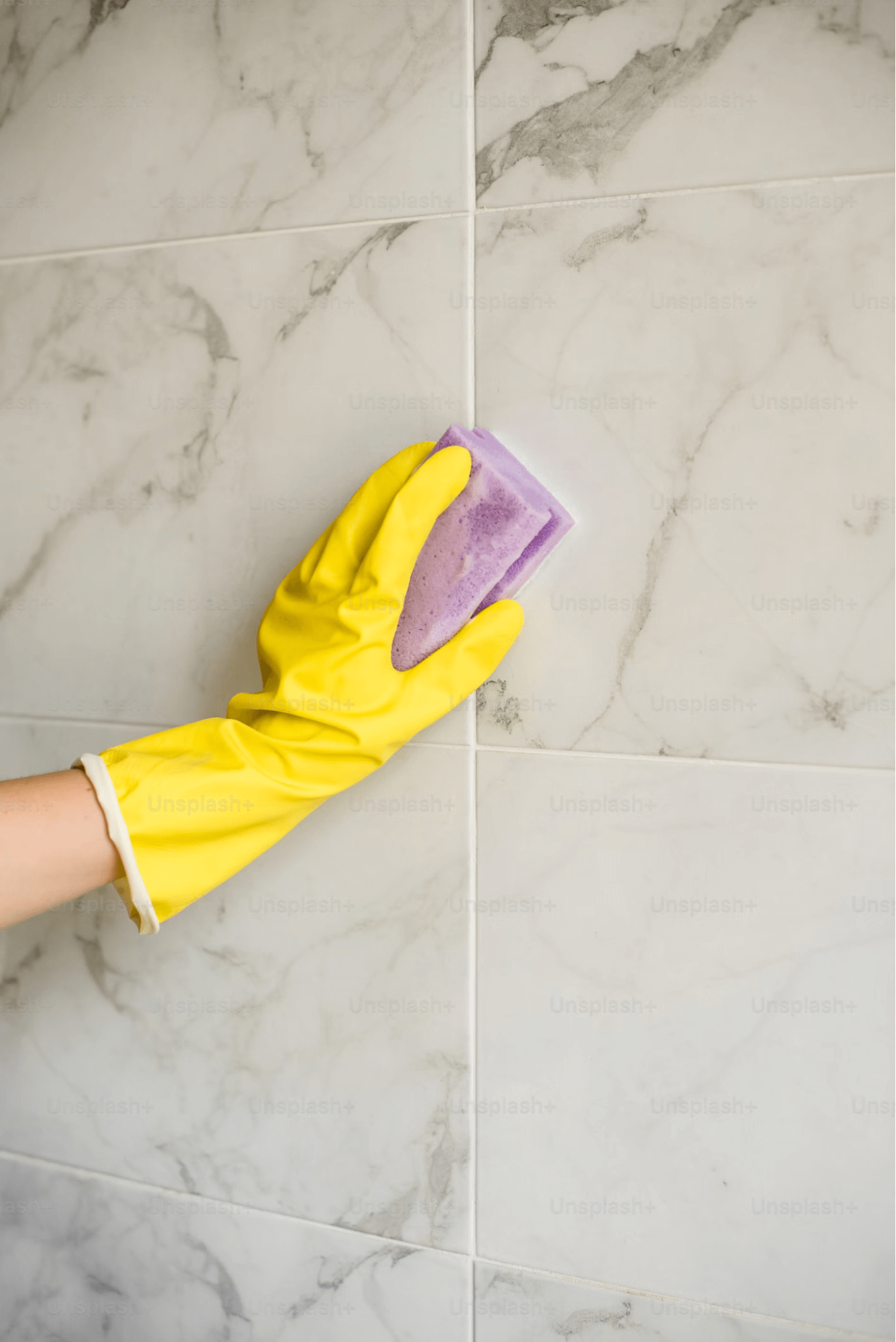A gloved hand scrubs a tile wall with a sponge