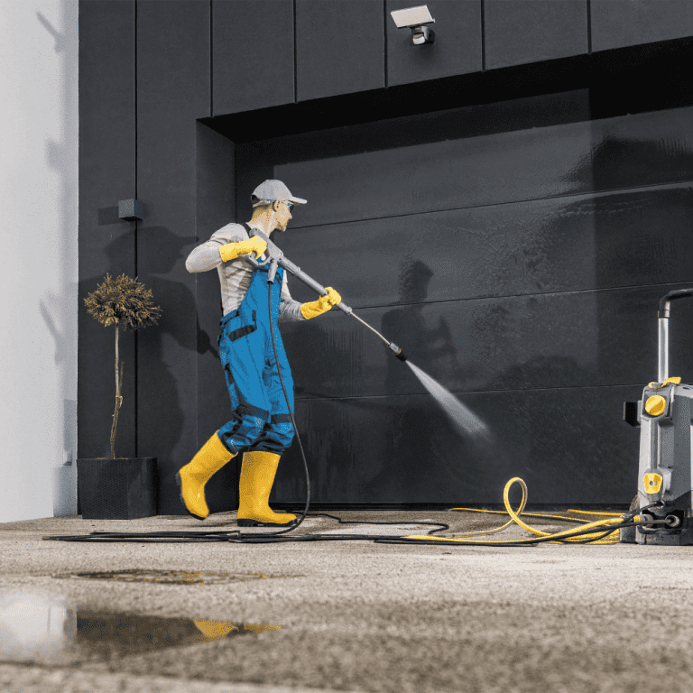 A professional in rubber boots and personal protective equipment pressure washes a commercial garage door