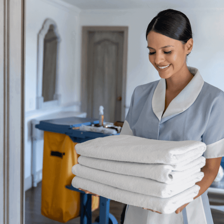 A hotel day porter happily carries a stack of four fresh white towels