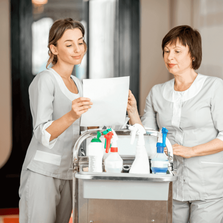 Two hotel day porters discuss their cleaning schedule next to a cleaning cart