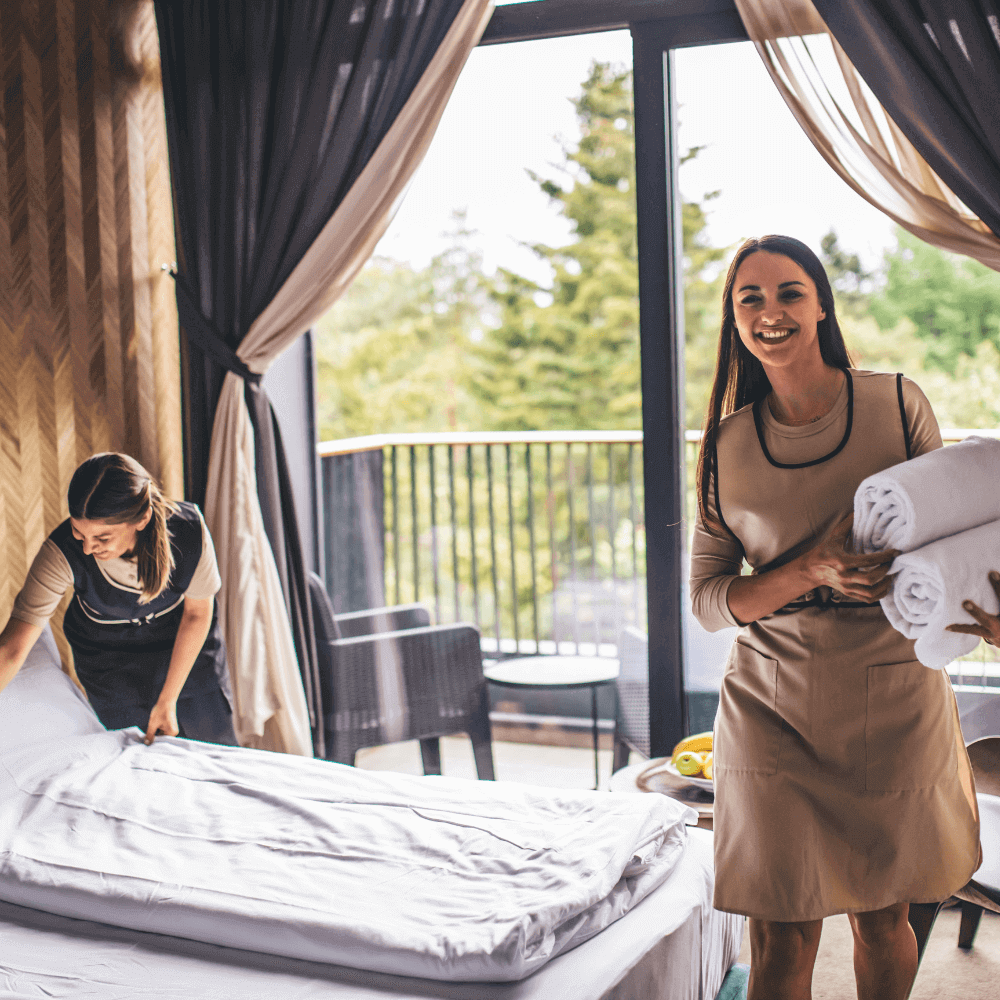 Two smiling day porters collaborate to strip a hotel bed and clean a room for the next guests.