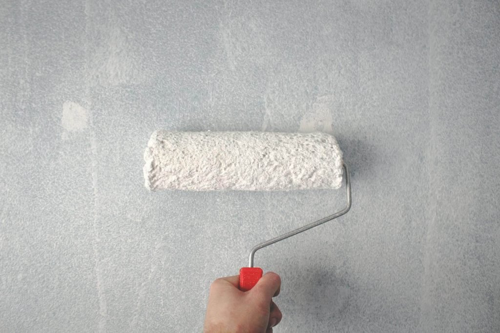 A professional painter rolls fresh white paint onto newly hung drywall