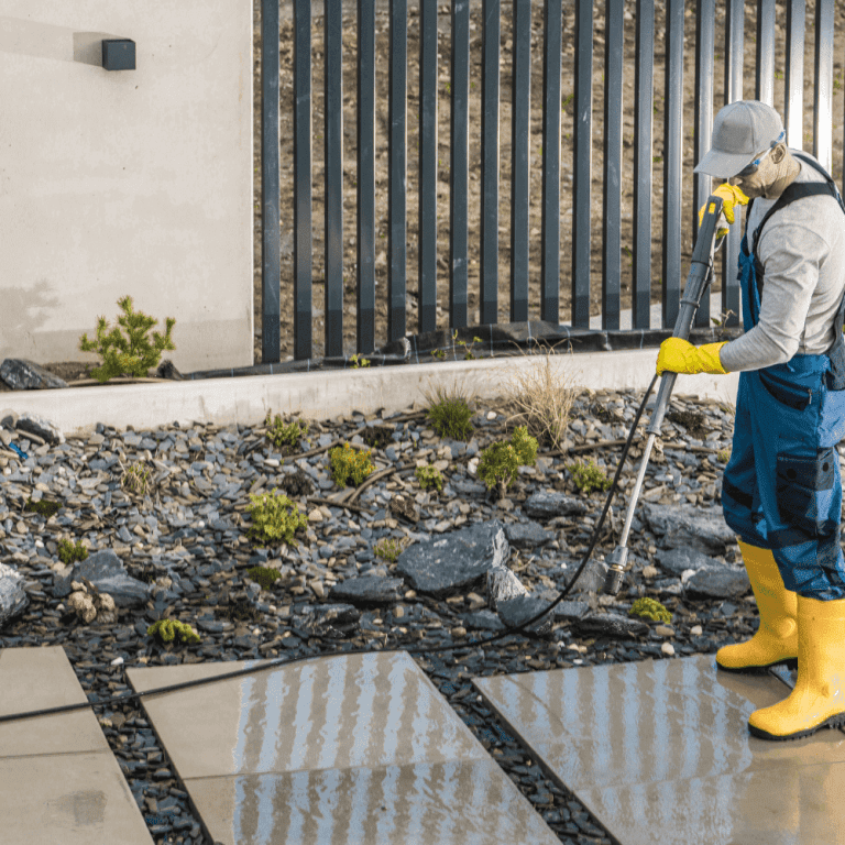 A professional in rubber boots and personal protective equipment performs pressure washing services in high-traffic areas outside a business