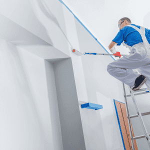 A professional painter on a ladder paints a high white wall with a roller