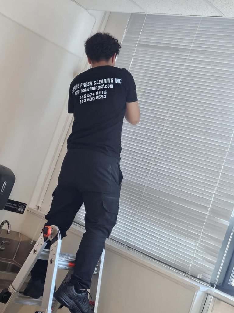 A janitor is cleaning the window blinds.
