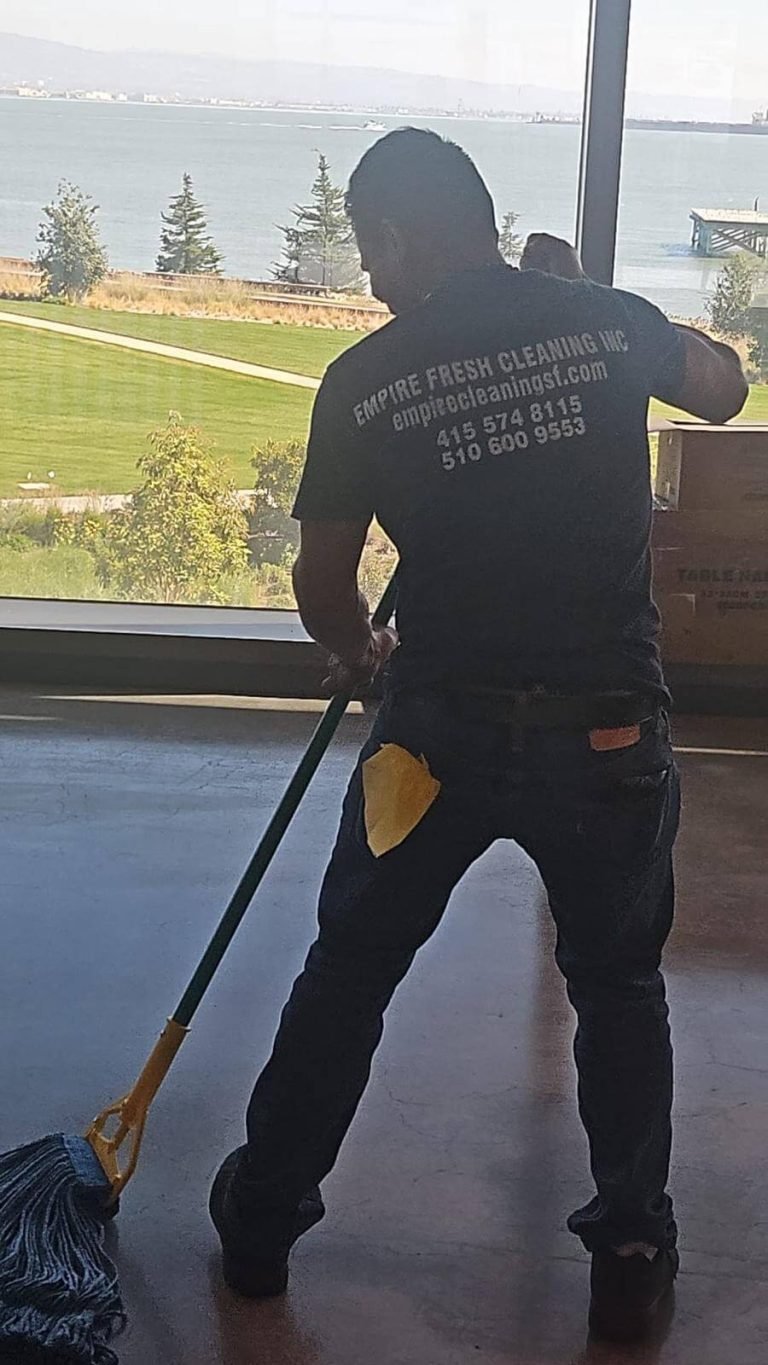 A janitor mops the floor in front of a window with a view of the San Francisco Bay